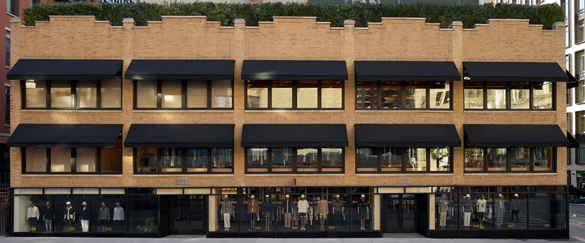 Fachada de ladrillo de la tienda insignia Kith Manhattan, con toldos negros y escaparates en la planta baja.