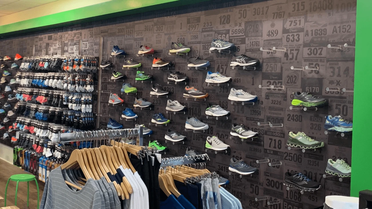 Running shoes on a race-number patterned wall beside socks and clothing racks.