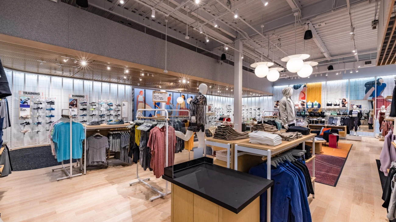 Nike store interior with sneaker walls, clothing displays and mannequins beneath globe lights.