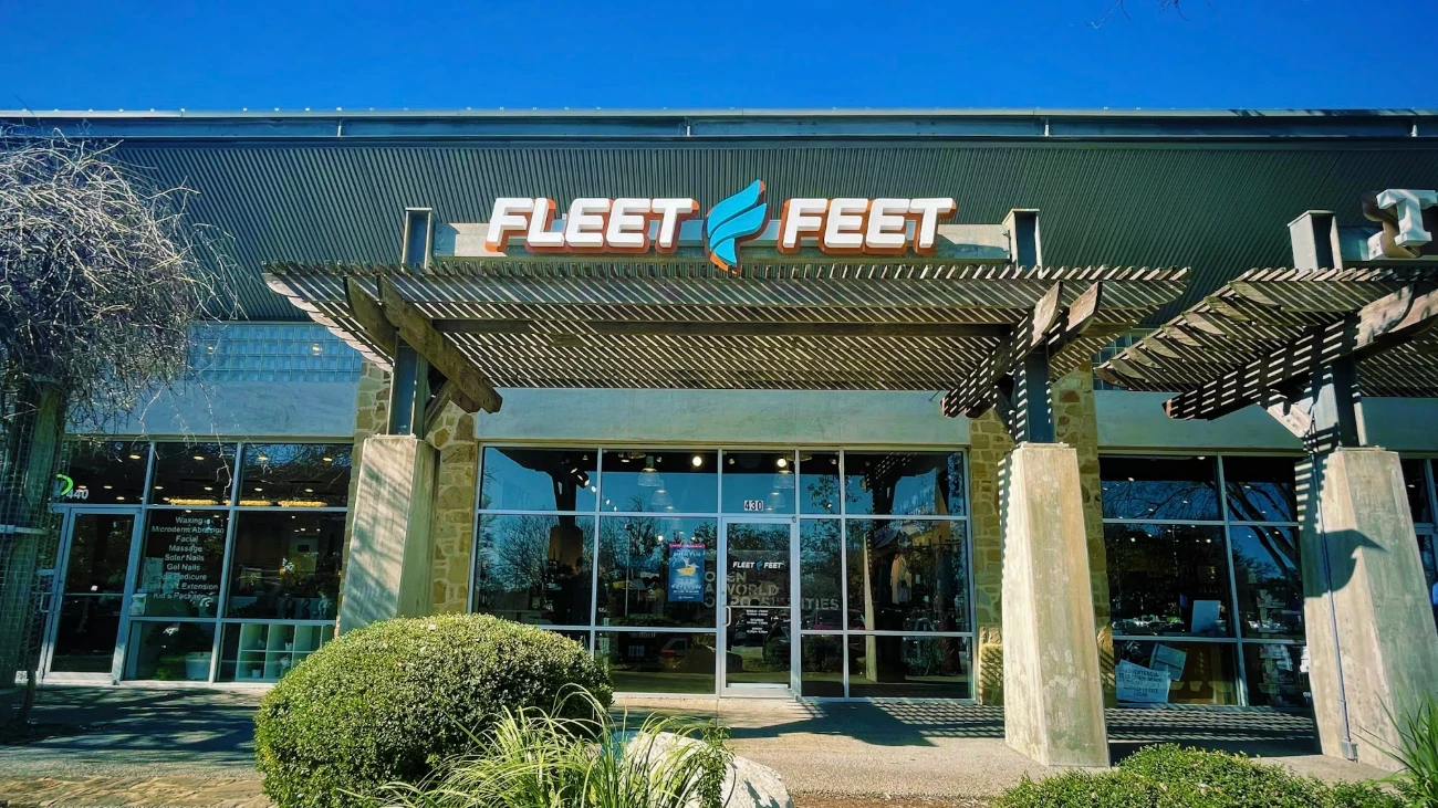 Fleet Feet storefront with a wooden pergola, glass doors and landscaping.