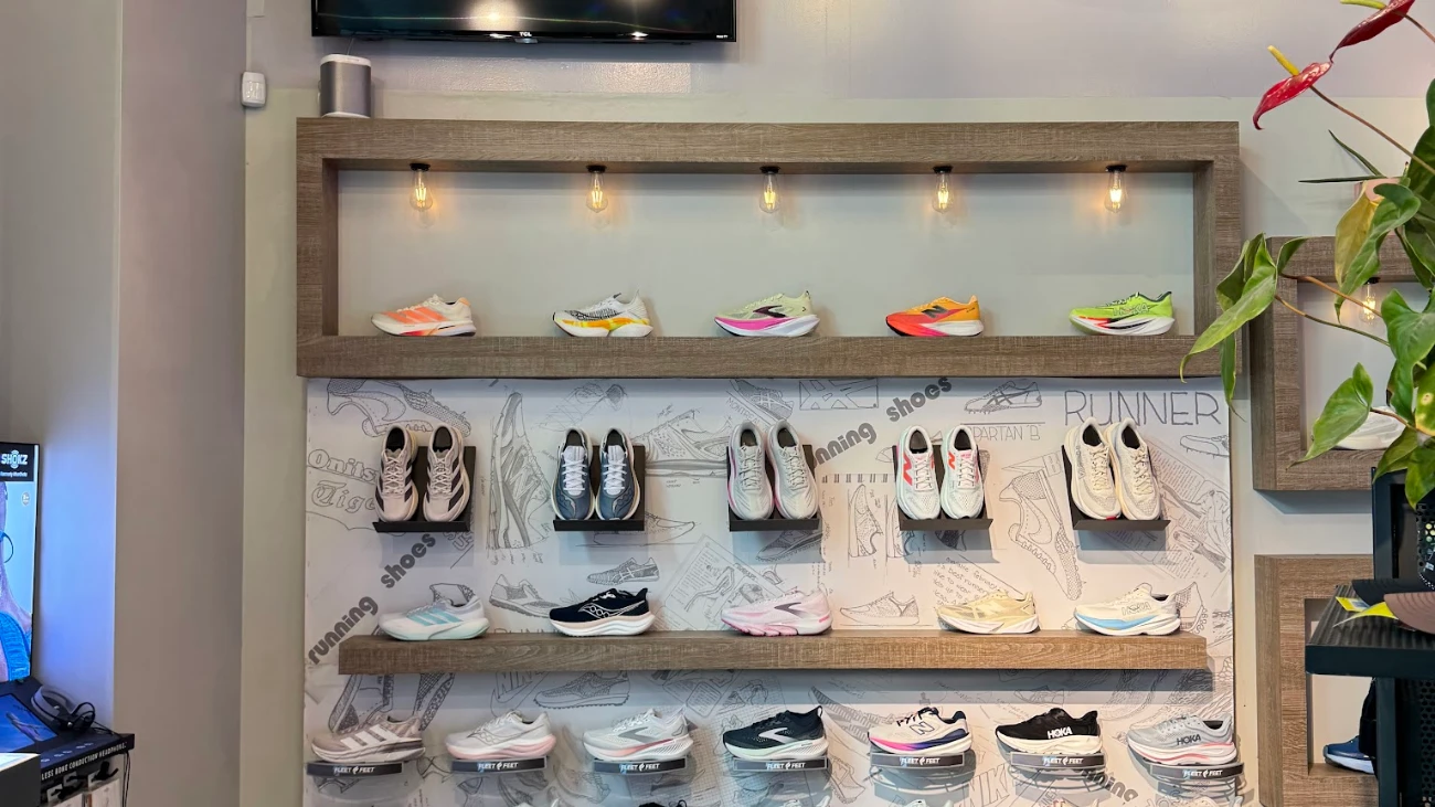 Running-shoe display framed in wood beneath exposed bulbs, with illustrated shoe wallpaper.