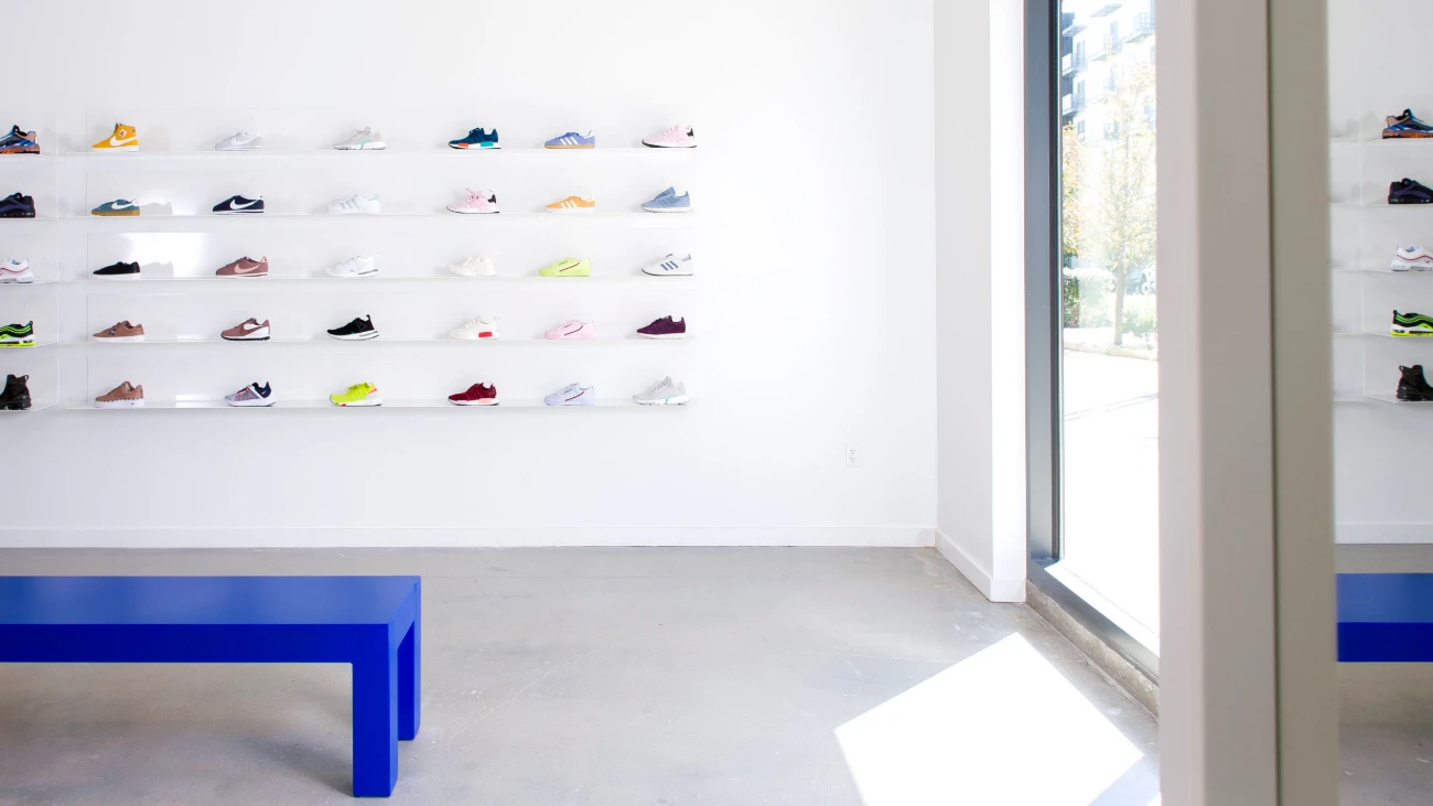Bright sneaker-display wall beside a blue bench and a tall street-facing window.