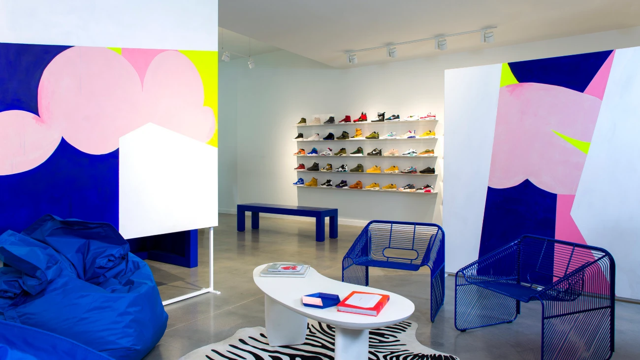 Sneaker-store seating area with blue chairs, colorful wall panels and shoe shelves in the background.