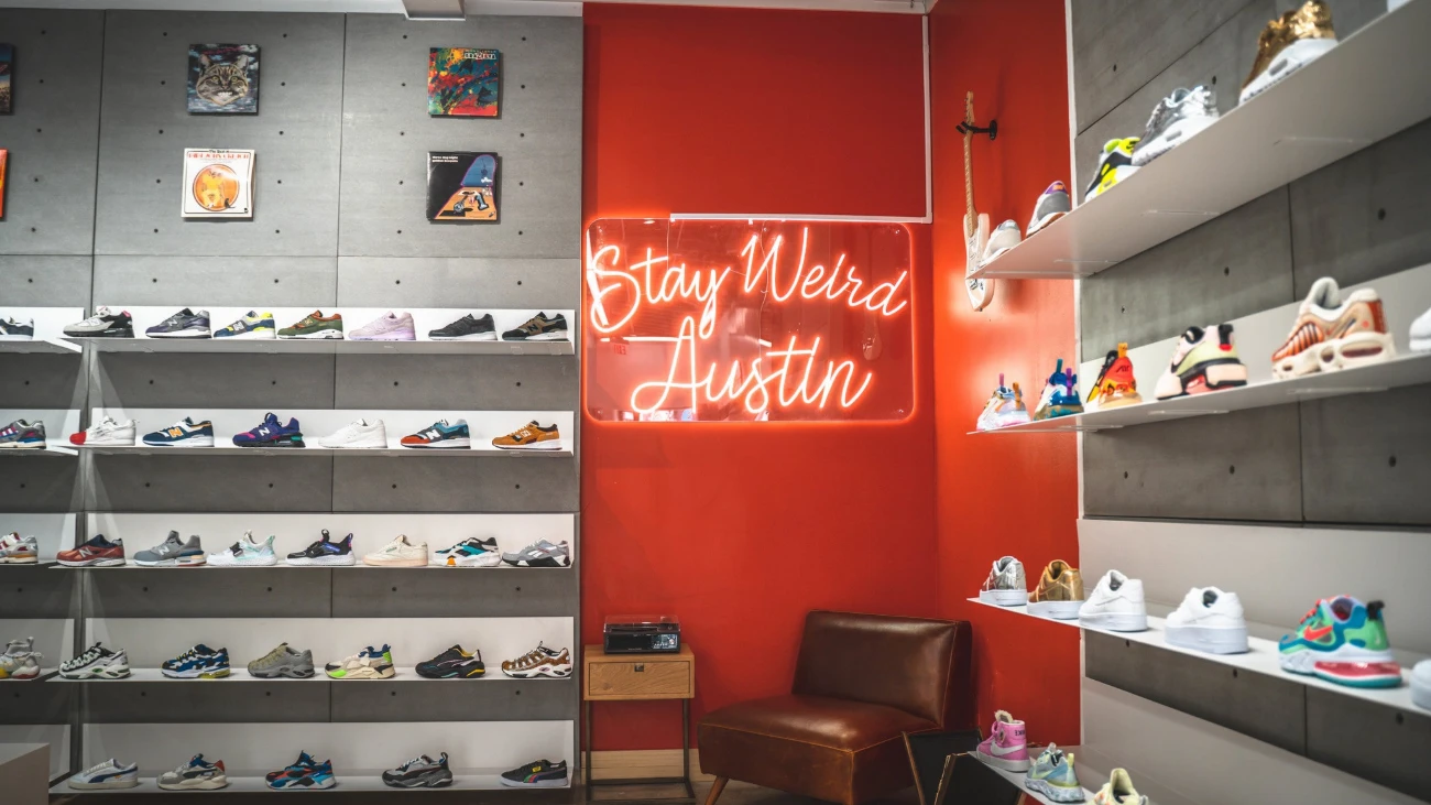 Sneaker shelves around a red wall with a Stay Weird Austin neon sign and a brown chair.