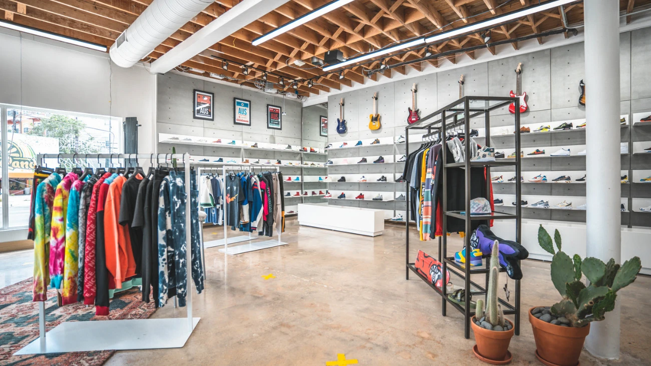 Sneaker-store interior with shoe-lined walls, electric guitars, clothing racks and potted cacti.