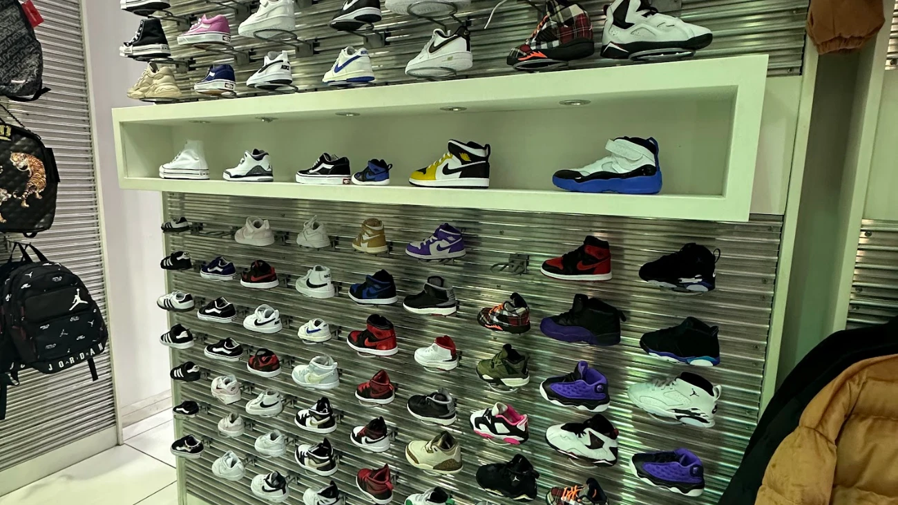 Rows of sneakers on a metal display wall with a white recessed shelf.