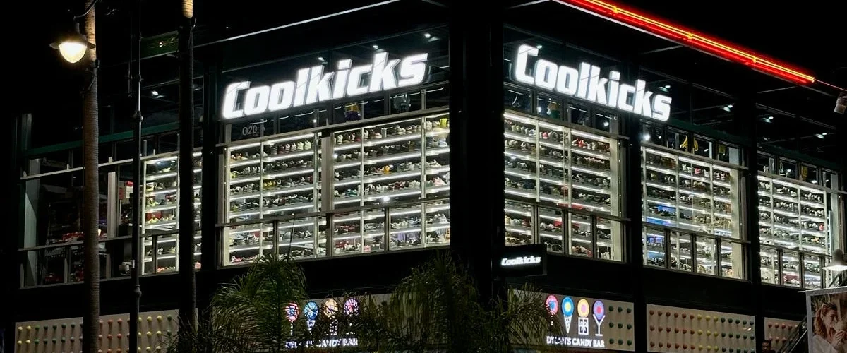 CoolKicks storefront at night in the Los Angeles Farmers Market, with illuminated signs and sneakers lining the windows.