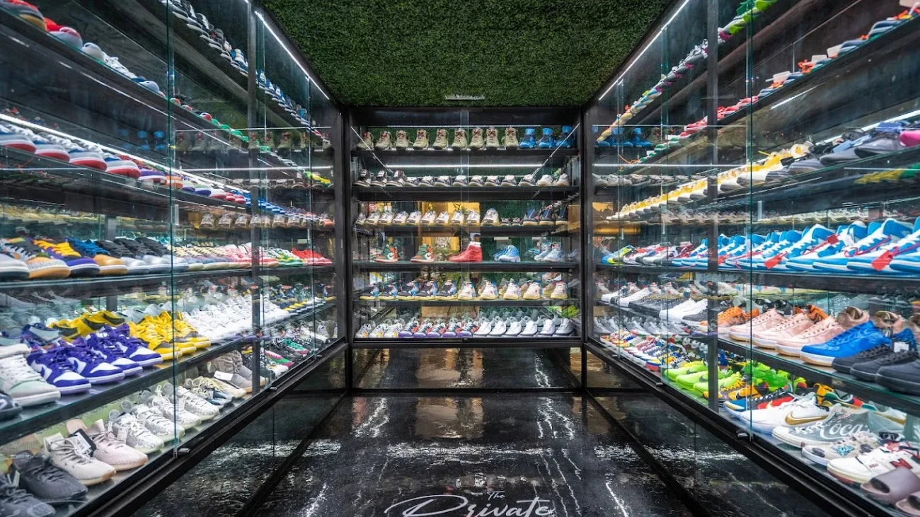 Glass-walled sneaker display room with dark floors and dense rows of colorful shoes