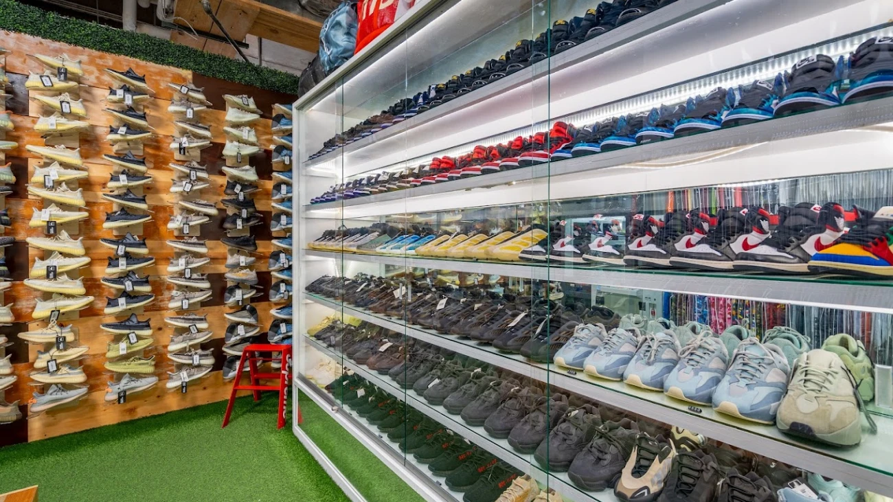 Sneakers displayed in illuminated glass cabinets beside a wooden shoe wall