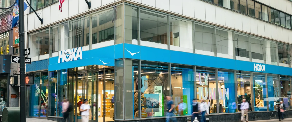 HOKA corner storefront on Fifth Avenue in New York, with blue signage and floor-to-ceiling windows.