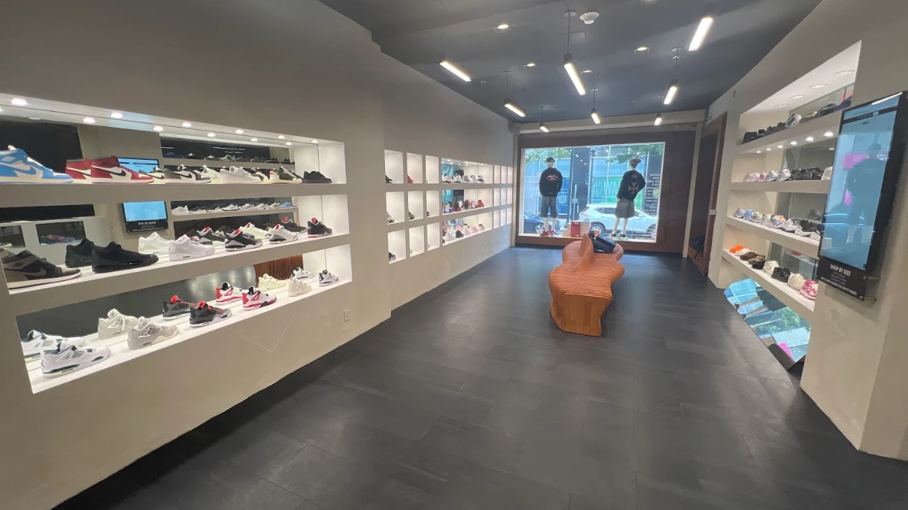 Narrow sneaker boutique with illuminated wall niches, dark flooring and a central sculptural bench.