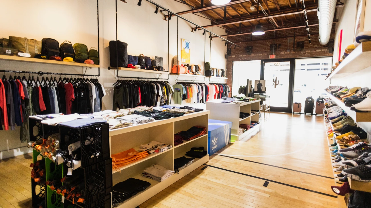 Bright boutique interior with wooden flooring, clothing racks and sneakers along a white wall.