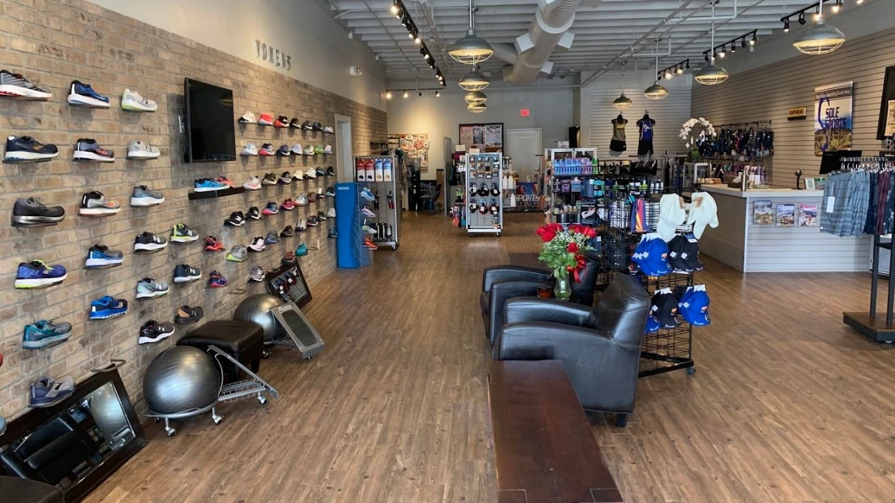 Running-store interior with a long shoe wall, black fitting chairs and wooden flooring.