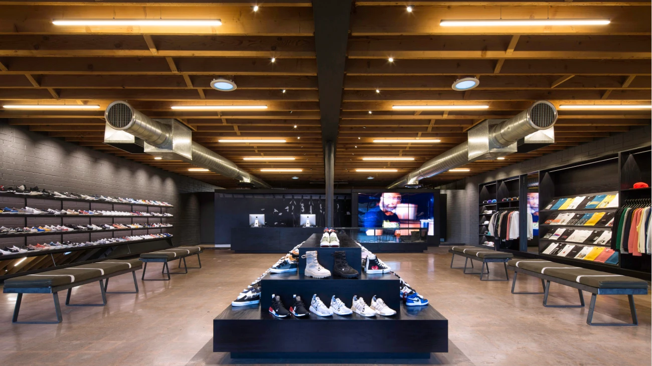 Sneaker boutique with a central stepped display, fitting benches and shoes along a dark wall.