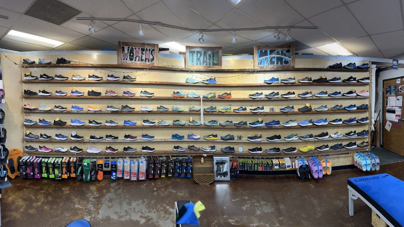 Long running-shoe wall beneath signs for women’s shoes, trail shoes and socks.