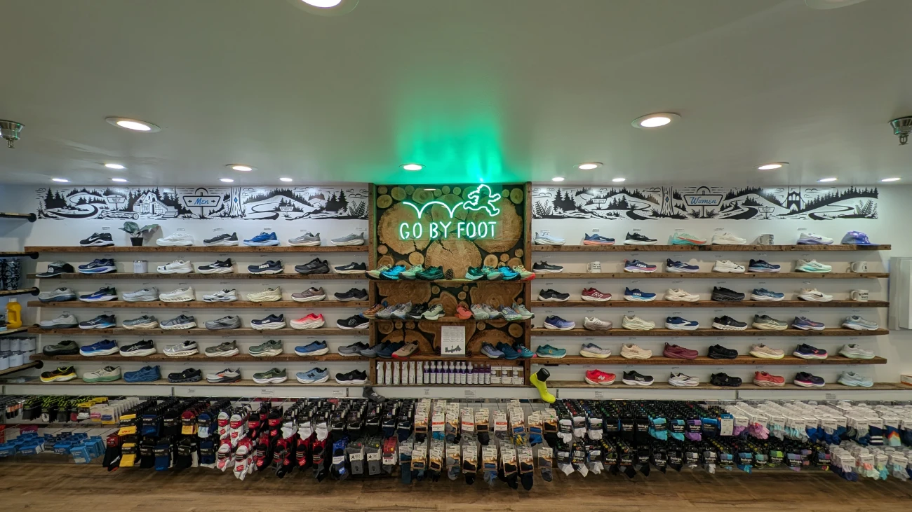 Running-shoe wall with a central Go by Foot sign and rows of accessories below.