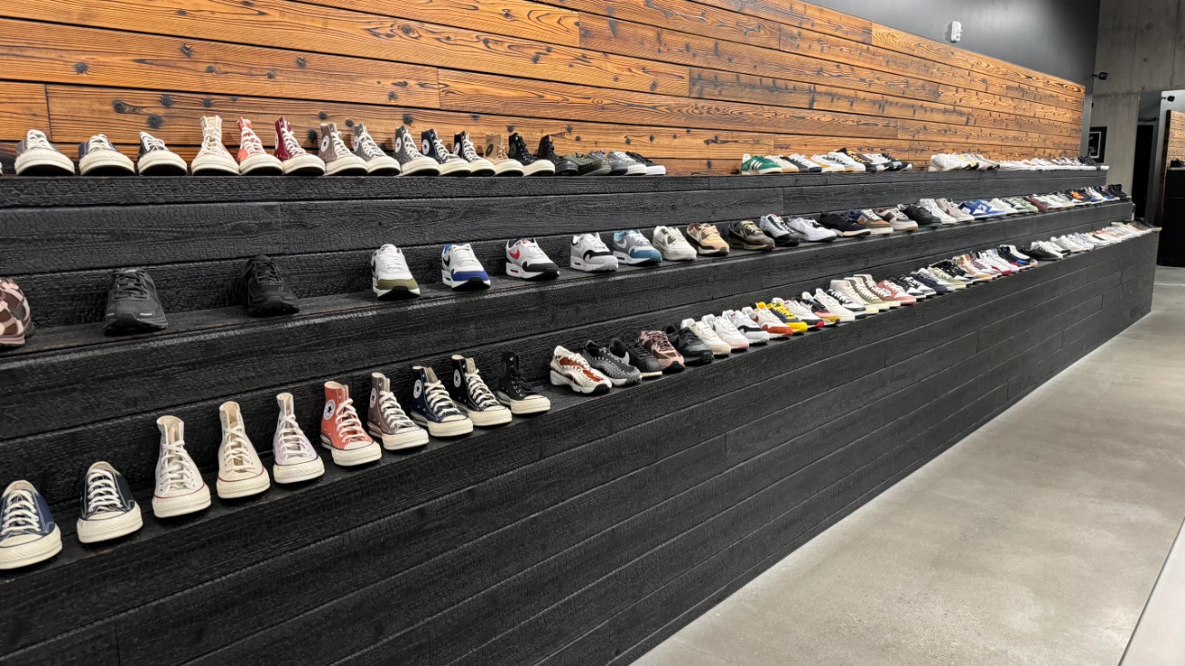 Long black stepped display of sneakers beneath a reclaimed-wood wall.