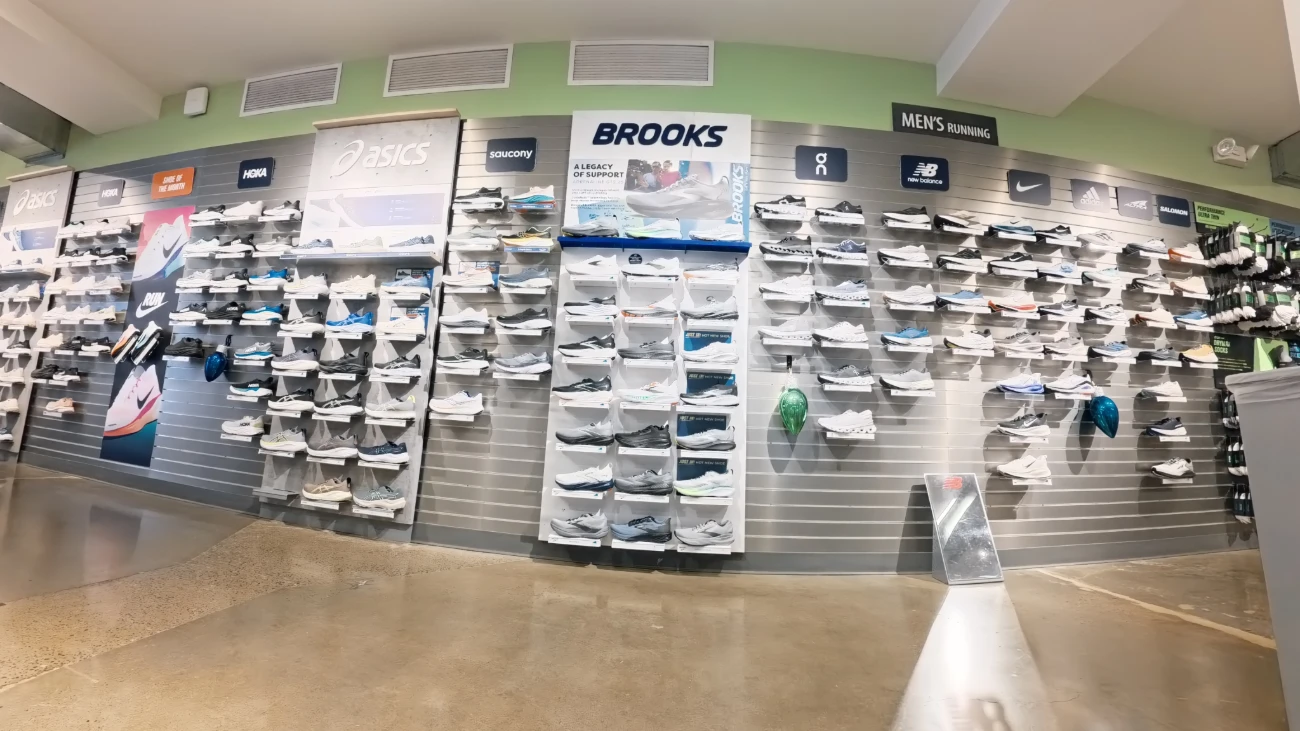 Wide running-shoe wall beneath Brooks, Asics and other sports-brand signs.