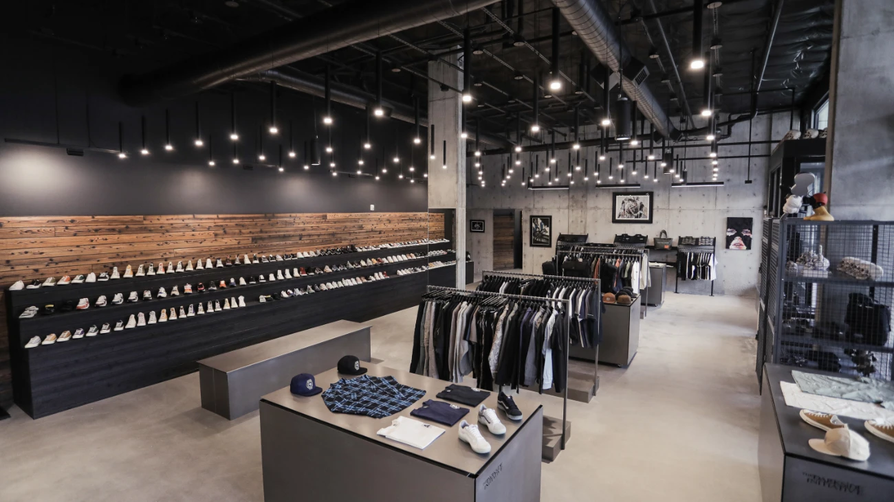 Industrial-style sneaker boutique with a long shoe wall, hanging lights and clothing racks.