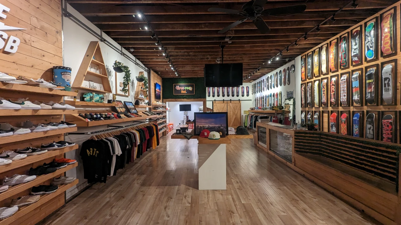 Wood-lined skate and sneaker shop with shoe shelves on one side and framed skateboard decks on the other.