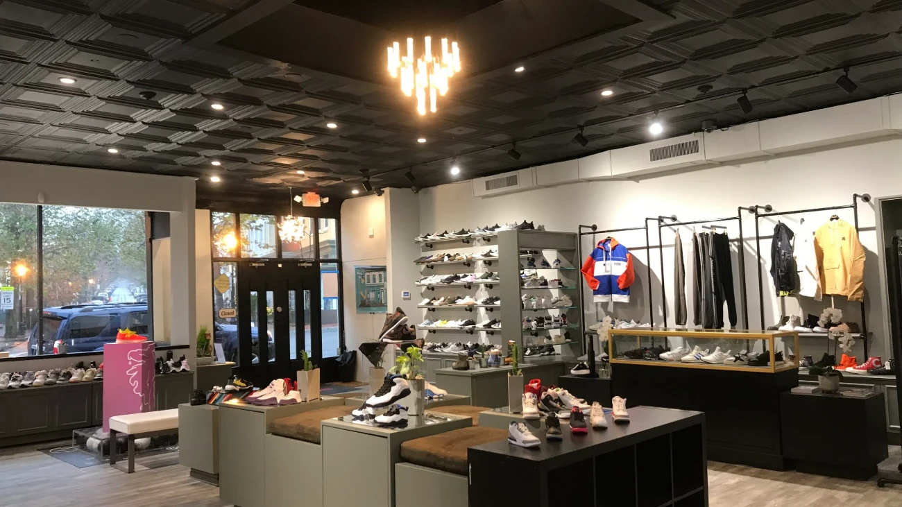Wide boutique interior with sneaker tables, clothing racks and street-facing windows.