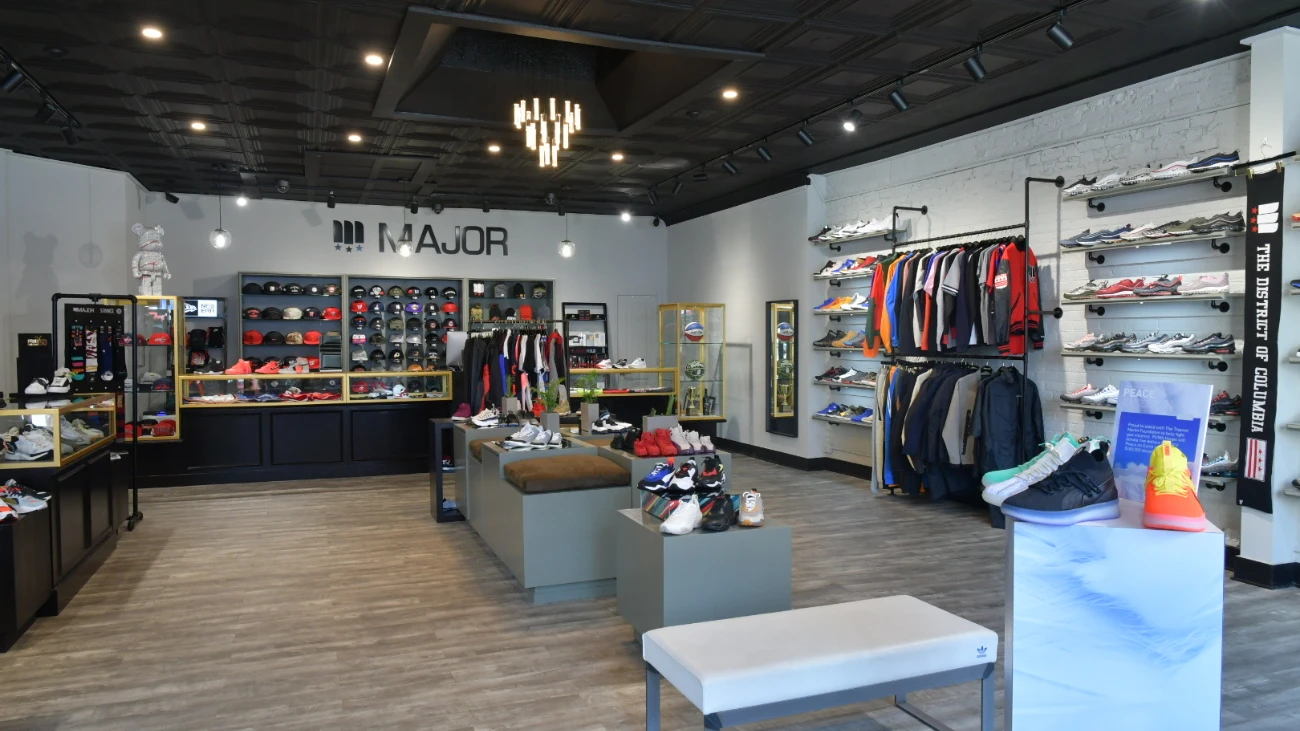 MAJOR sneaker boutique with shoe displays, clothing racks and a wall of caps beneath its logo.