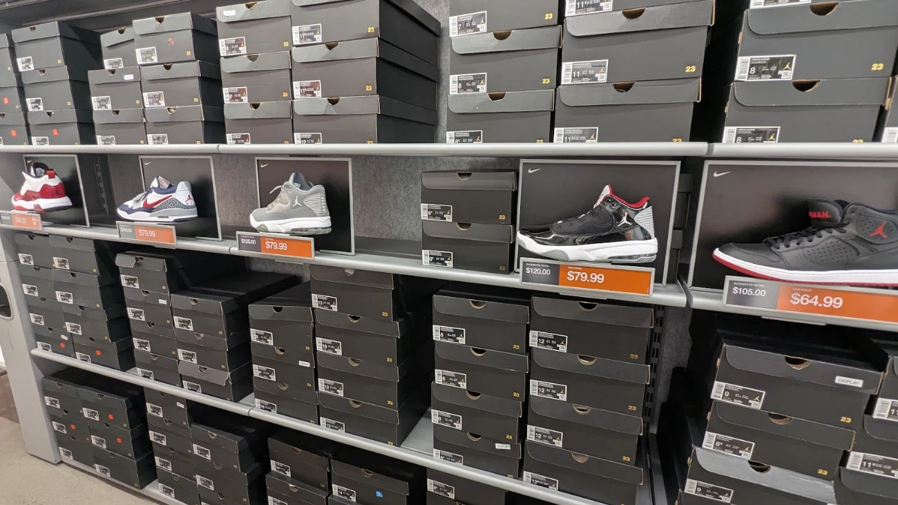 Nike and Jordan shoes displayed above rows of gray shoeboxes in an outlet aisle.