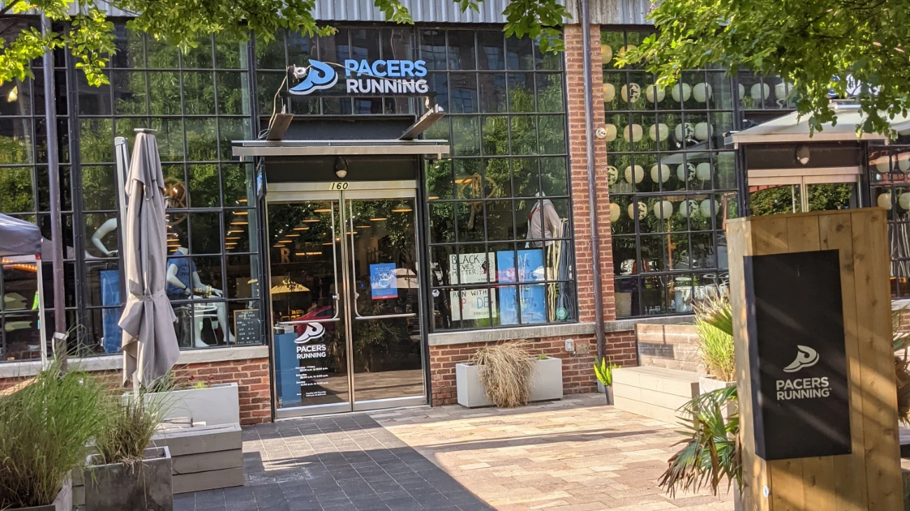Pacers Running storefront framed by brickwork, plants and outdoor seating.